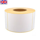 Single roll of white direct thermal labels with yellow backing paper, sitting upright on a white surface